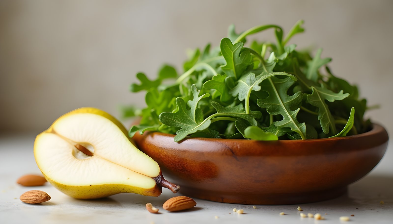 Arugula fiber shown with a wooden bowl piled with fresh arugula leaves beside a halved pear and a few whole almonds